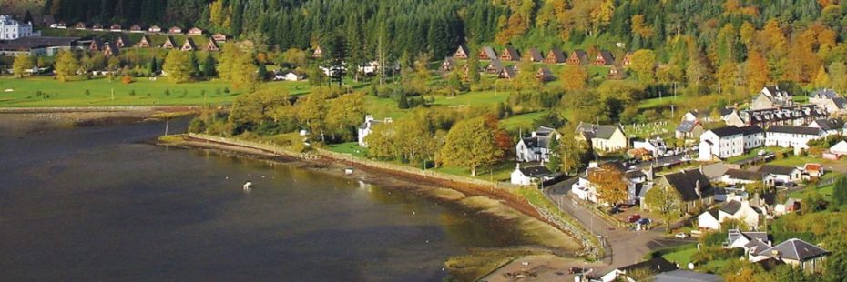 lochgoilhead-village-in-sunshine-surrounded-by-greenery-and-holiday-chalets-on-shore-of-loch-goil