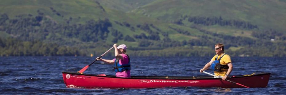 two-people-in-kayak-on-loch-forest-mountain-background