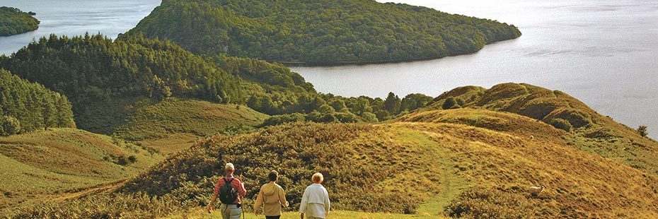 three-walkers-descending-conic-hill-slopes-in-sunset-light-with-inchcailloch-island-on-loch-lomond-visible-in-the-distance