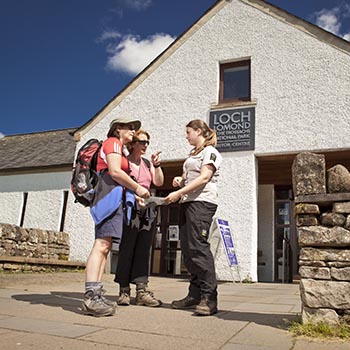 national-park-ranger-advising-two-women-walkers-in-front-of-balmaha-visitor-centre-on-blue-skies-summer-day