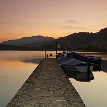 ferry-pier-at-sunset-at-lake-of-menteith-with-moored-boats-one-end-and-hills-in-the-distance