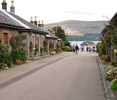 luss-pier-road-loch-lomond-in-distance-tourists-walking-pretty-houses-with-flowers-outside-on-both-sides