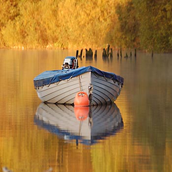 moored-boat-on-mirror-like-water-surface-with-autumn-tree-colours-behind