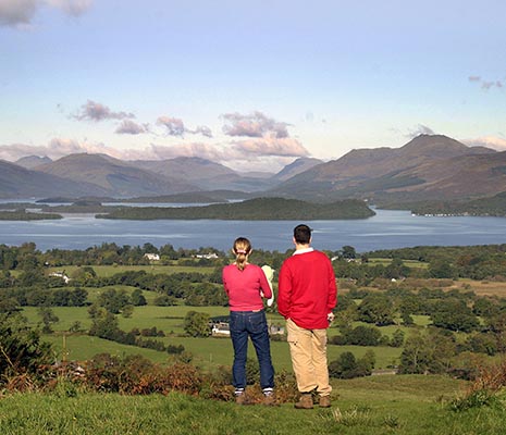 couple-with-baby-on-summit-of-dumpling-hill-in-gartocharn-adimiring-stunning-views-over-loch-lomond-islands-and-mountains