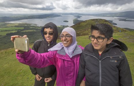 woman-wearing-white-hijab-and-glasses-and-with-two-young-boys-with-glasses-takes-selfie-loch-lomond-visible-behind-them-and-blue-banner-underneath-reads-our-vision