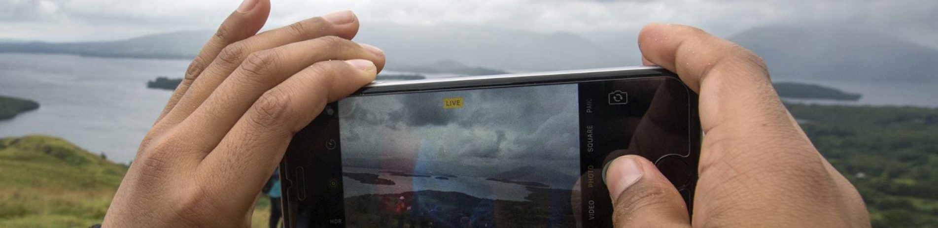 close-up-of-pair-of-hands-holding-smartphone-and-taking-photo-of-loch-lomond-and-its-islands