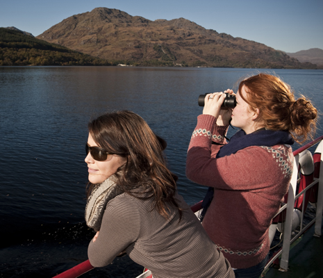 loch lomond day visit two-women-on-boat-deck-look-over-loch-lomond-water-one-through-binoculars