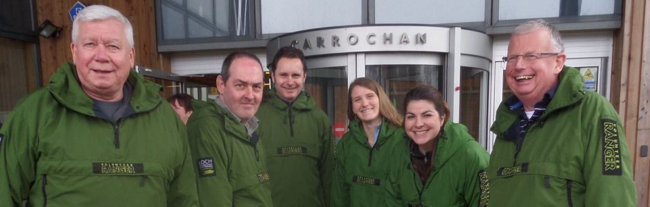 six-national-park-volunteer-rangers-in-green-jackets-and-smiling-at-camera-outside-headquarters