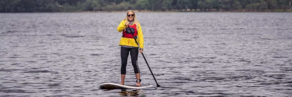 blonde-woman-with-sunglasses-and-smiling-paddleboarding-on-loch