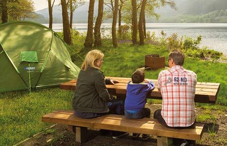 family-couple-with-young-boy-sit-at-picnic-table-next-to-large-green-tent-at-edge-of-loch-lubnaig