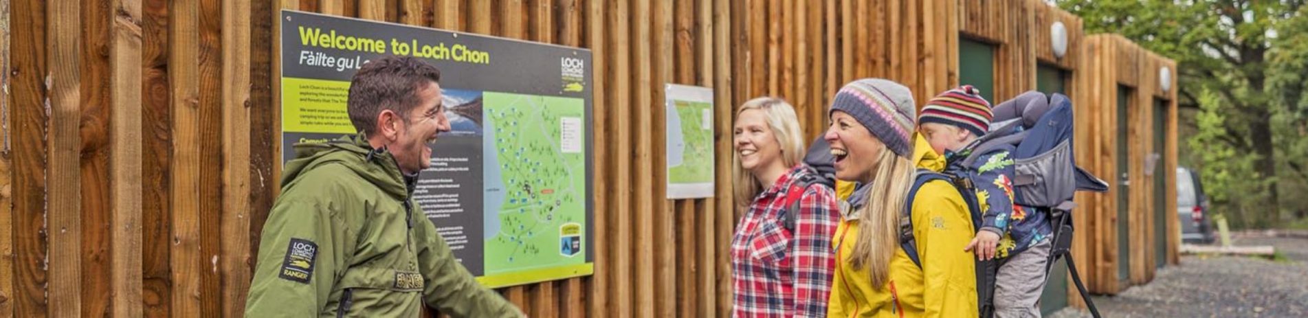 ranger-in-green-jacket-talking-enthusiastically-to-two-blonde-women-one-with-a-baby-on-her-back-at-the-loch-chon-campsite