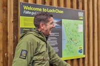 national-park-ranger-in-green-jacket-laughing-in-front-of-loch-chon-campsite-map