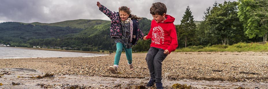 two-young-children-boy-and-girl-jumping-happily-in-stream-on-ardentinny-beach