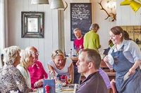 busy-tearoom-with-smiling-shop-assistant-chatting-to-seated-group