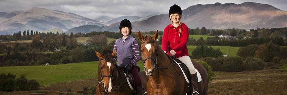 two-women-horseriding-with-conic-hill-and-farmland-behind-them