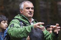 national-park-ranger-in-green-jacket-demonstrating-something-using-his-hands-in-front-of-school-students-in-the-forest