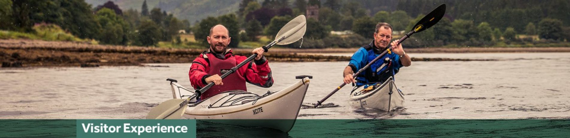 two-men-one-in-red-the-other-in-blue-peddling-in-separate-kayaks-on-loch-long-with-ardentinny-in-the-distance-blue-banner-underneath-reading-visitor-experience