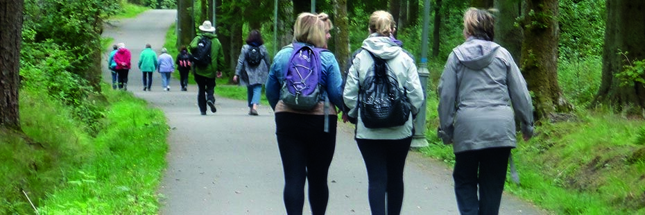 group-of-people-walking-on-path-in-the-forest-with-four-women-two-of-them-with-small-backpacks-prominent-in-the-foreground