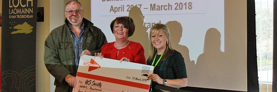 national-park-staff-and-multiple-sclerosis-society-reps-holding-cheque-from-national-park-with-charity-donation-and-smiling-at-camera