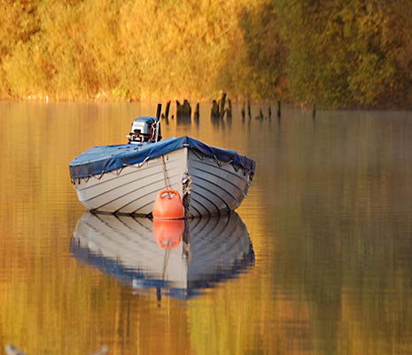 moored-boat-on-mirror-like-water-surface-with-autumn-tree-colours-behind