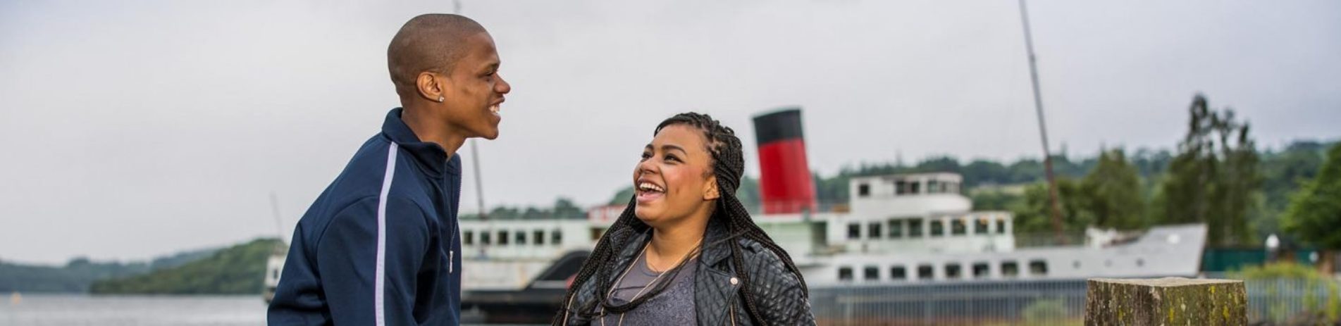 young-black-couple-laughing-at-edge-of-loch-lomond-with-maid-of-loch-steamship-behind