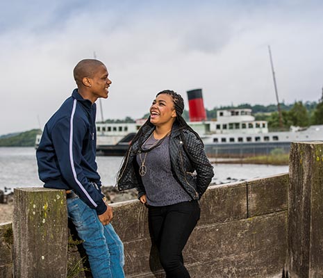 young-black-couple-laughing-at-edge-of-loch-lomond-with-maid-of-loch-steamship-behind