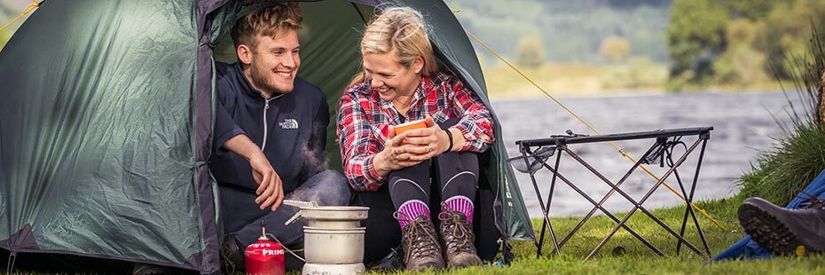 young-blond-camping-smiling-cooking-at-entrance-of-green-tent-on-shore-of-loch-chon