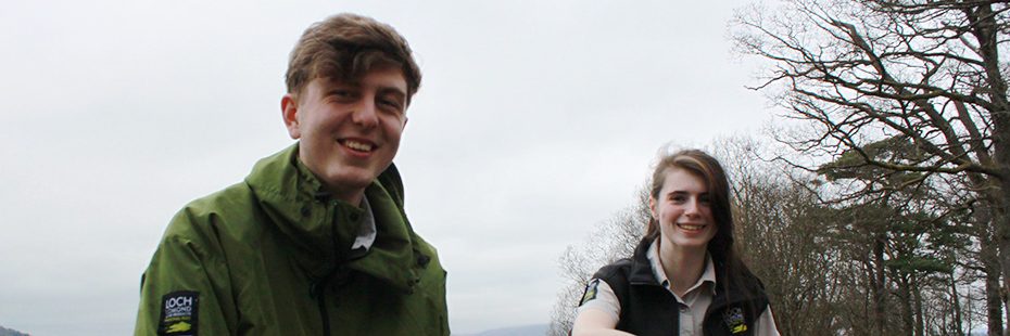 thomas-and-eilidh-national-park-young-apprentices-posing-smiling-at-edge-of-loch-lomond-in-balloch-wearing-national-park-branded-jackets