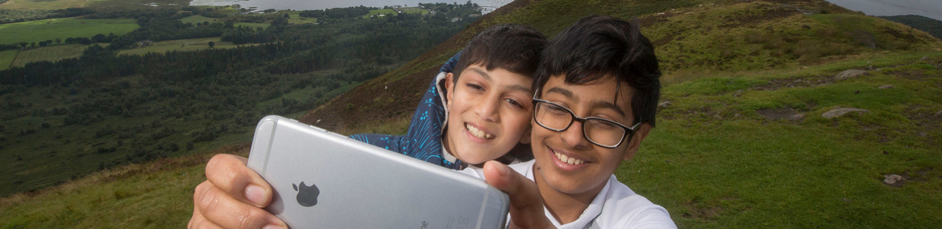 two-young-boys-smiling-and-taking-a-selfie-on-conic-hill-with-loch-lomond-behind