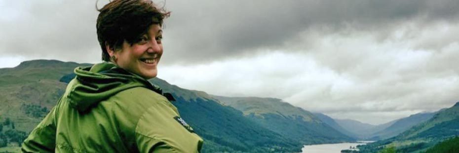 emma-white-volunteer-with-national-park-short-reddish-hair-smiling-with-green-jacket-against-landscape-of-loch-and-hills