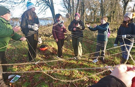 young-volunteers-wrapped-up-warm-in-a-circle-in-the-forest-with-ropes-in-the-air-in-between-them-and-passing-a-ball-through-the-air