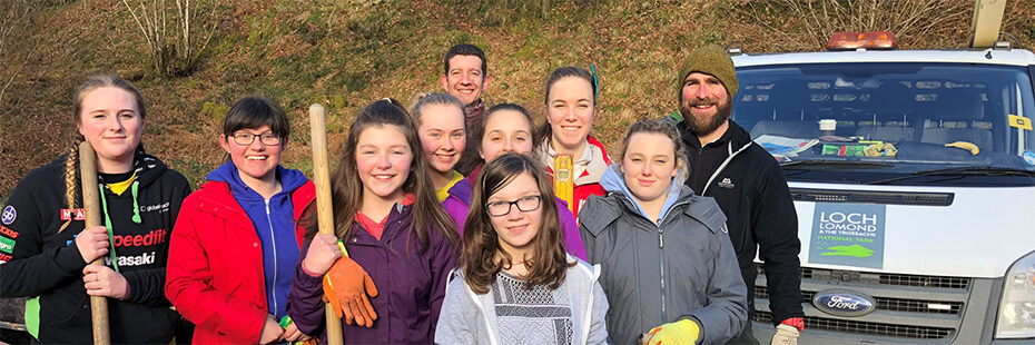 group-of-school-girls-volunteers-holding-spades-alongside-two-national-park-land-operations-staff-next-to-white-van