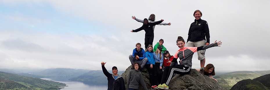 group-of-young-people-and-national-park-education-officer-on-summit-of-ben-aan-with-loch-katrine-and-trossachs-behind