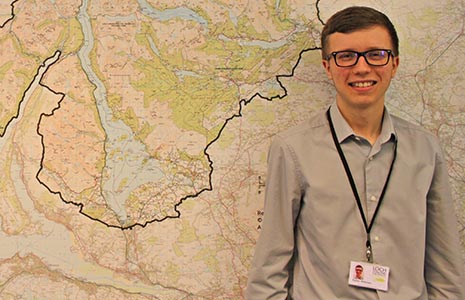 national-park-young-staff-male-with-glasses-smiling-at-camera-next-to-national-park-map