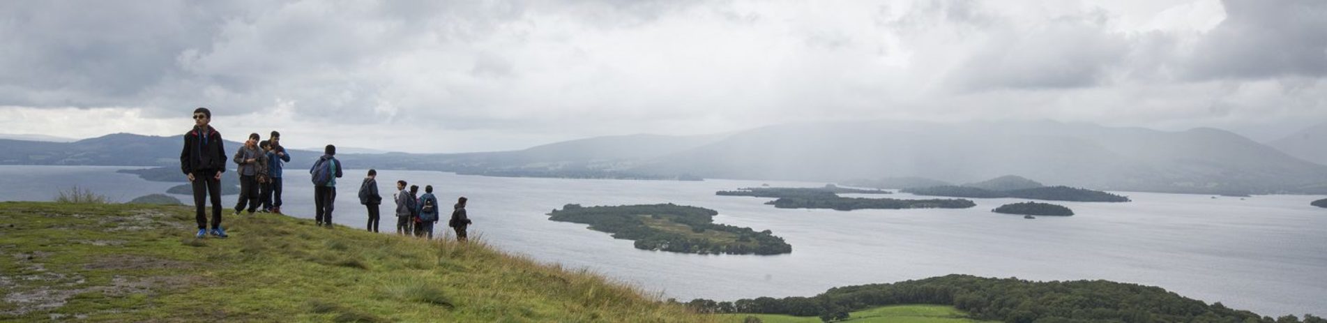 group-of-boys-on-conic-hill-with-stunning-view-of-loch-lomond-and-islands-dark-clouds-above
