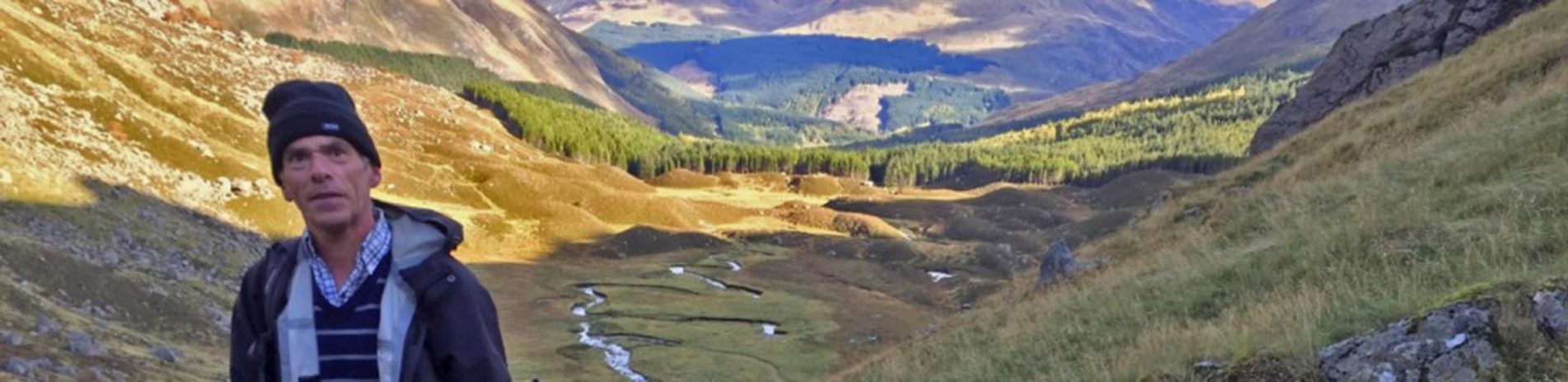 euan-ramage-national-park-volunteer-holding-spade-on-mountain-track-restoration-with-lush-landscape-behind