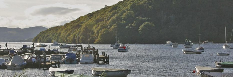 view-of-boats-moored-in-balmaha-on-loch-lomond-with-wooded-inchcailloch-in-the-distance