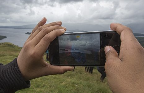 close-up-of-hands-holding-smartphone-and-taking-photo-of-stunning-landscape-from-conic-hill