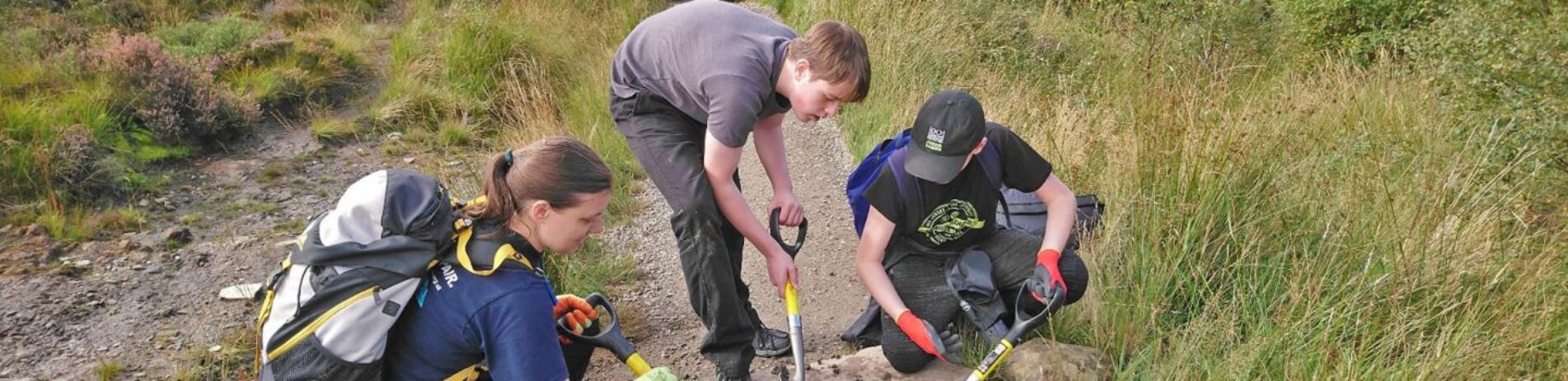 two-male-junior-rangers-with-spades-and-woman-clearing-drain-during-path-repair-exercise-as-part-of-their-john-muir-award