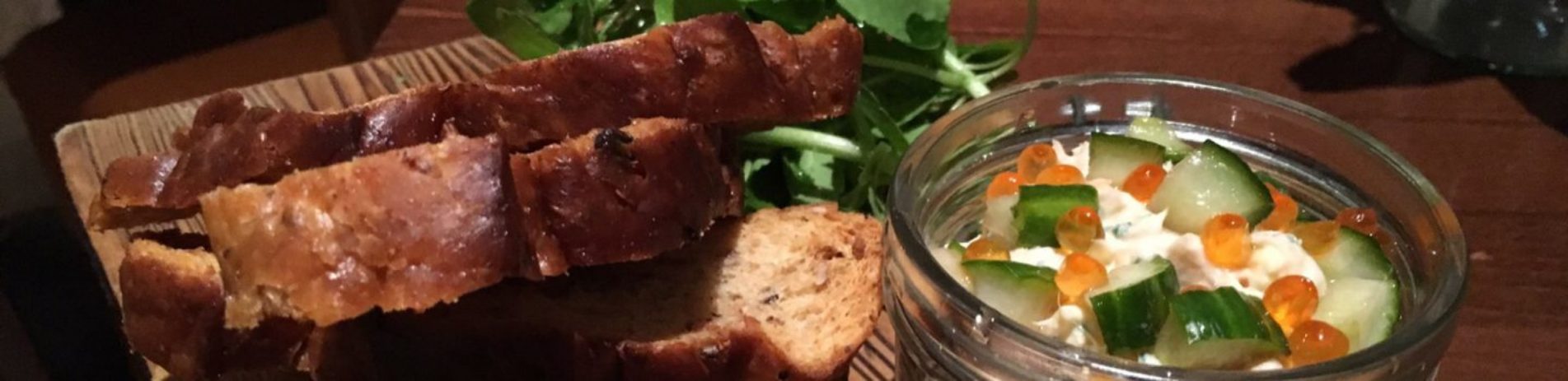 salmon-pate-in-open-glass-jar-on-wooden-board-next-to-bread-slices-and-fresh-herbs