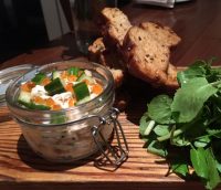 salmon-pate-in-open-glass-jar-on-wooden-board-next-to-bread-slices-and-fresh-herbs