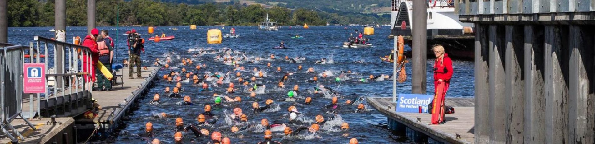 great-scottish-swim-event-seen-from-balloch-slipway-dozens-of-swimmers-with-green-and-orange-caps-swimming-vigorously