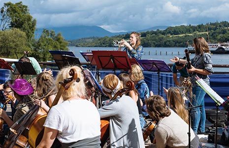 orchestra-playing-at-lomond-shores-balloch-with-loch-lomond-and-maid-of-the-loch-steamship-visible-behind-balloch-festival-two-thousand-eighteen