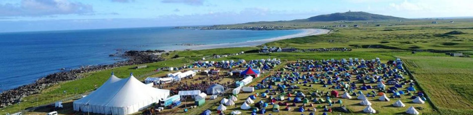 aerial-view-tiree-festival-grounds-with-huge-white-tents-cars-and-and-people-and-beaches-sea-on-left-and-green-fields-on-right