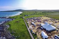 aerial-view-tiree-festival-grounds-with-huge-white-tents-cars-and-and-people-and-beaches-sea-on-left-and-green-fields-on-right