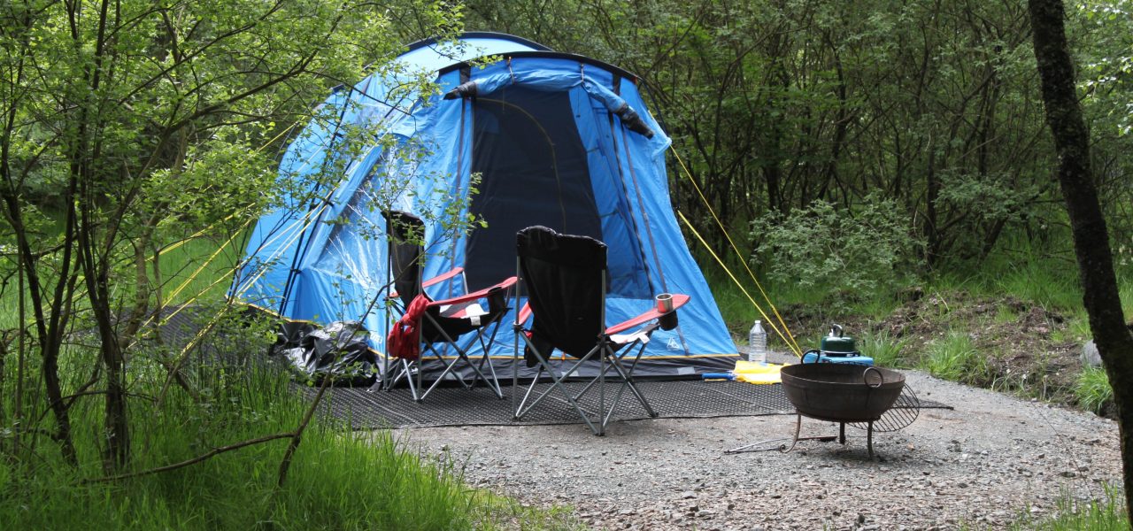 loch-chon-campsite-pitch-number-twenty-five-large-blue-tent-pitched-with-two-folding-chairs-outside-as-well-as-fire-bowl-and-trees-surrounding-it