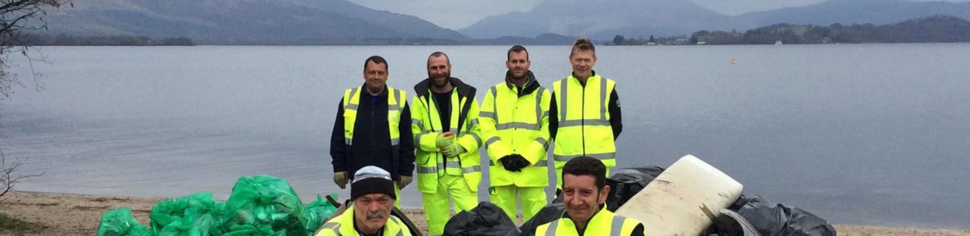 six-men-dressed-in-high-viz-clothes-with-dozens-of-bin-bags-aligned-in-front-of-them-on-the-edge-of-loch-lomond-from-spring-clean-campaign