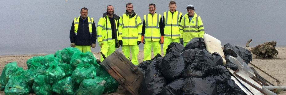 six-men-dressed-in-high-viz-clothes-with-dozens-of-bin-bags-aligned-in-front-of-them-on-the-edge-of-loch-lomond-from-spring-clean-campaign