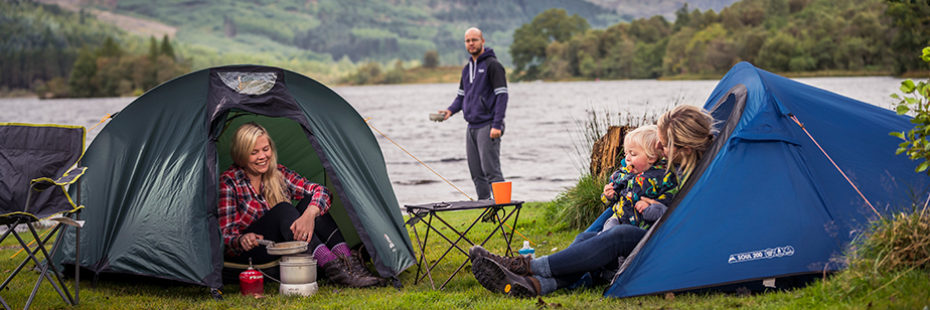 campers-in-two-tents-cooking-by-loch-chon-one-lady-sits-at-the-entrance-of-one-tent-holding-a-pot-above-a-gas-stove-while-the-other-lady-at-the-entrance-of-the-other-tent-is-holding-a-baby-a-man-behind-the tent-is-bringing-some-water-in-a-metal-bowl