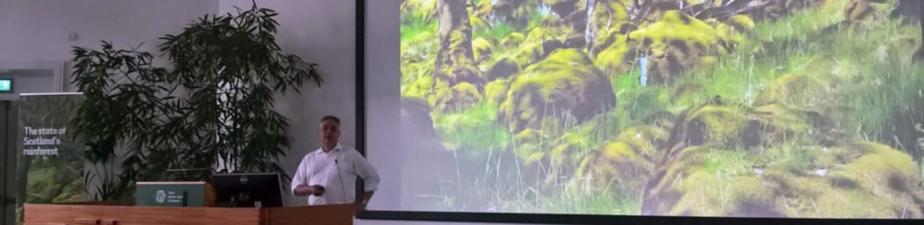 older-male-dressed-in-white-giving-a-presentation-using-microphone-and-screen-on-a-conservation-topic